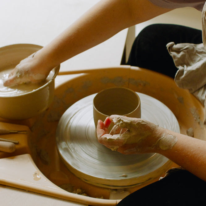 Hands shaping clay on a potter's wheel during a beginner wheel class, focusing on creating pottery pieces.