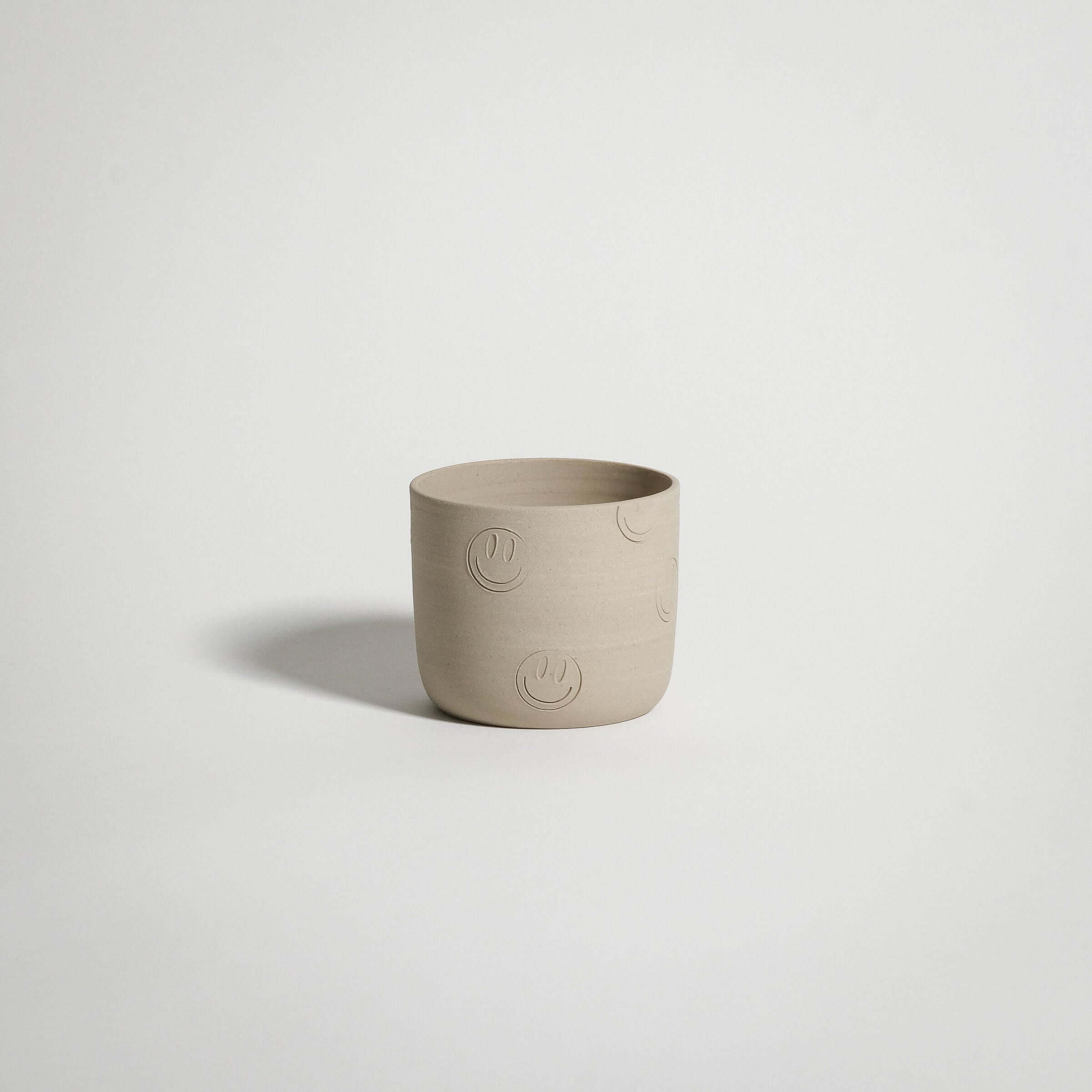 Smiley coffee cup made from grey stoneware with smiley face stamps and glossy interior glaze.