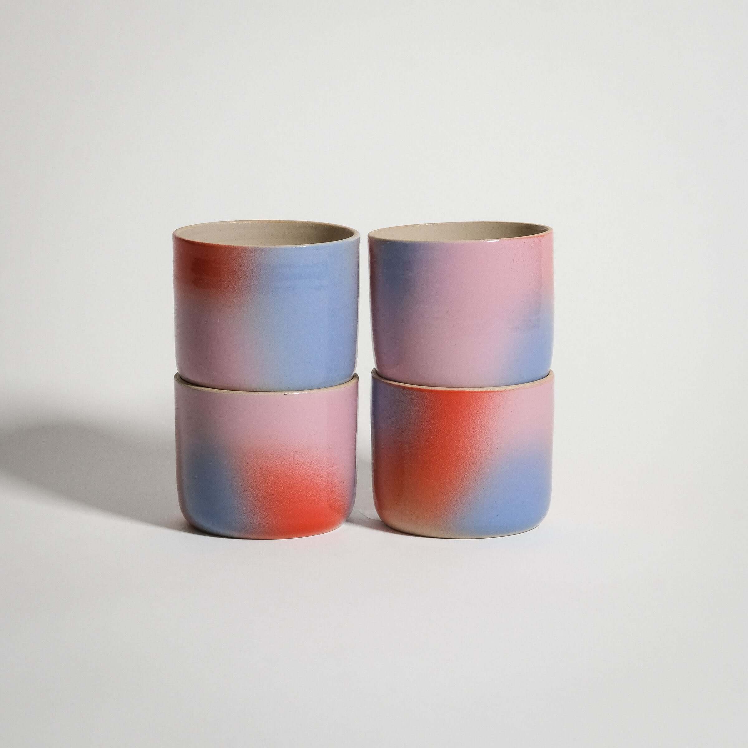 Stacked wheel-thrown Dawn coffee cups in a red, blue, and lilac gradient, made from grey stoneware.