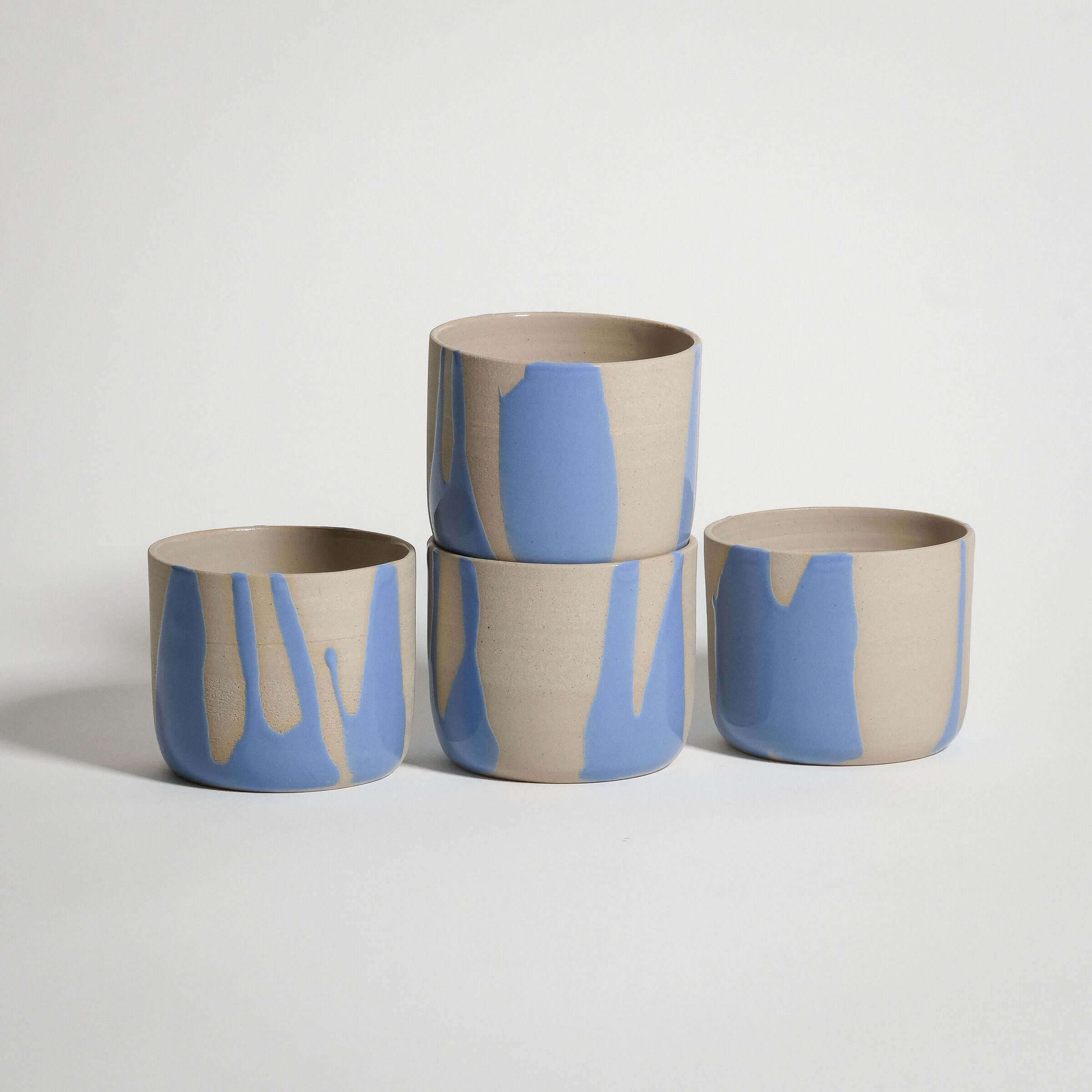 Handcrafted blue stoneware cups, wheel-thrown with glossy glazes, stacked for display on a neutral background.