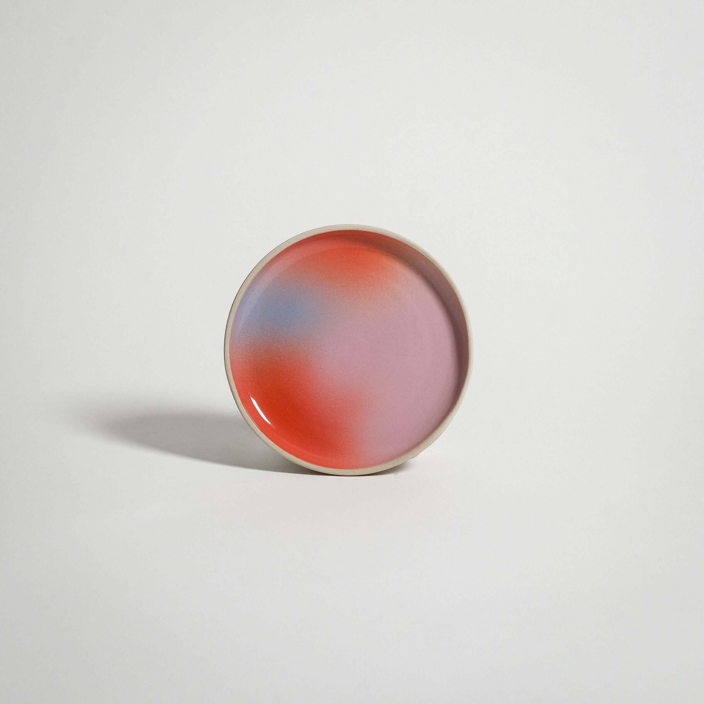Handcrafted grey stoneware small plate featuring a red, blue, and lilac spray-painted gradient.