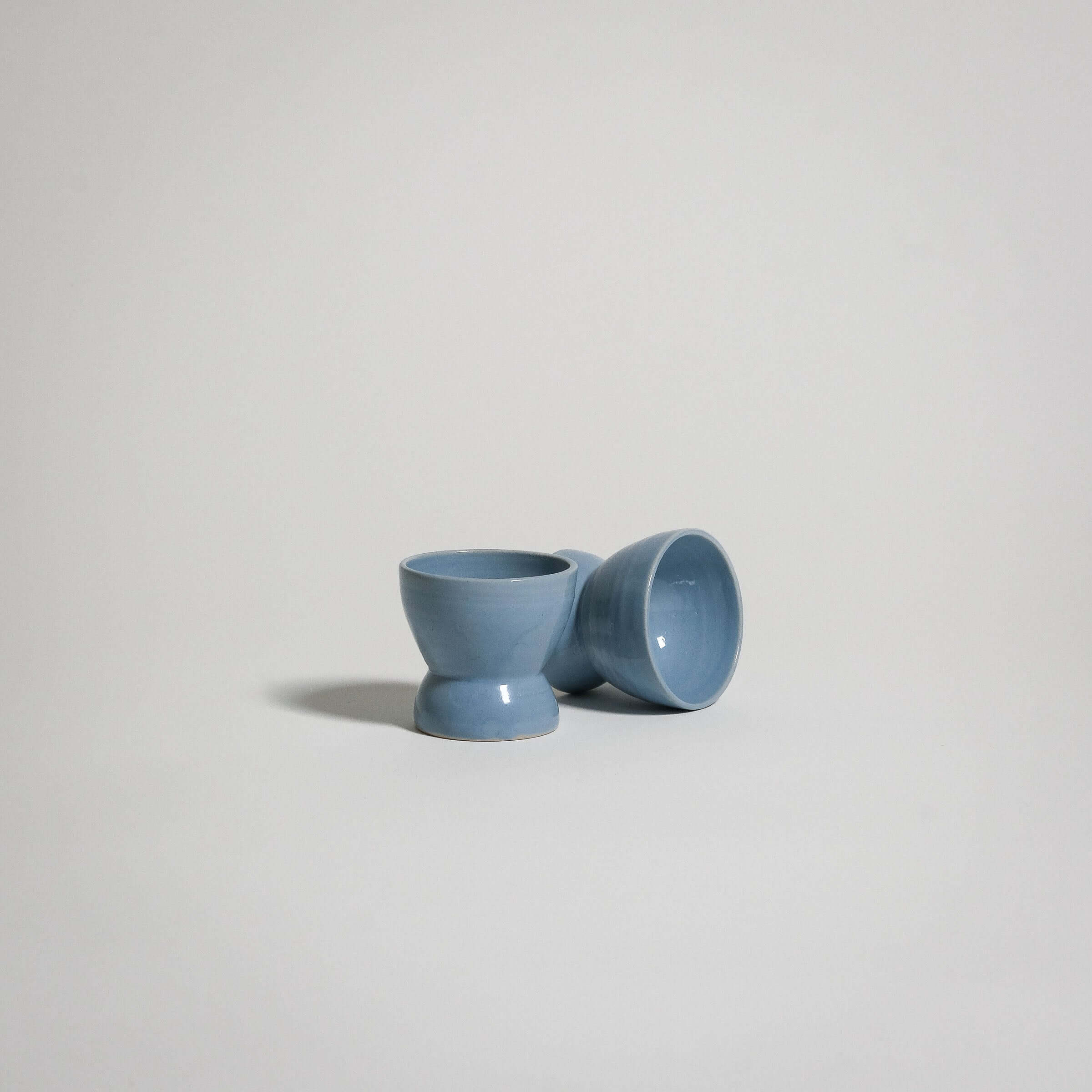 A classic ceramic Egg Cup in the color ice blue. Two are on the picture, one is standing and one is laying down.