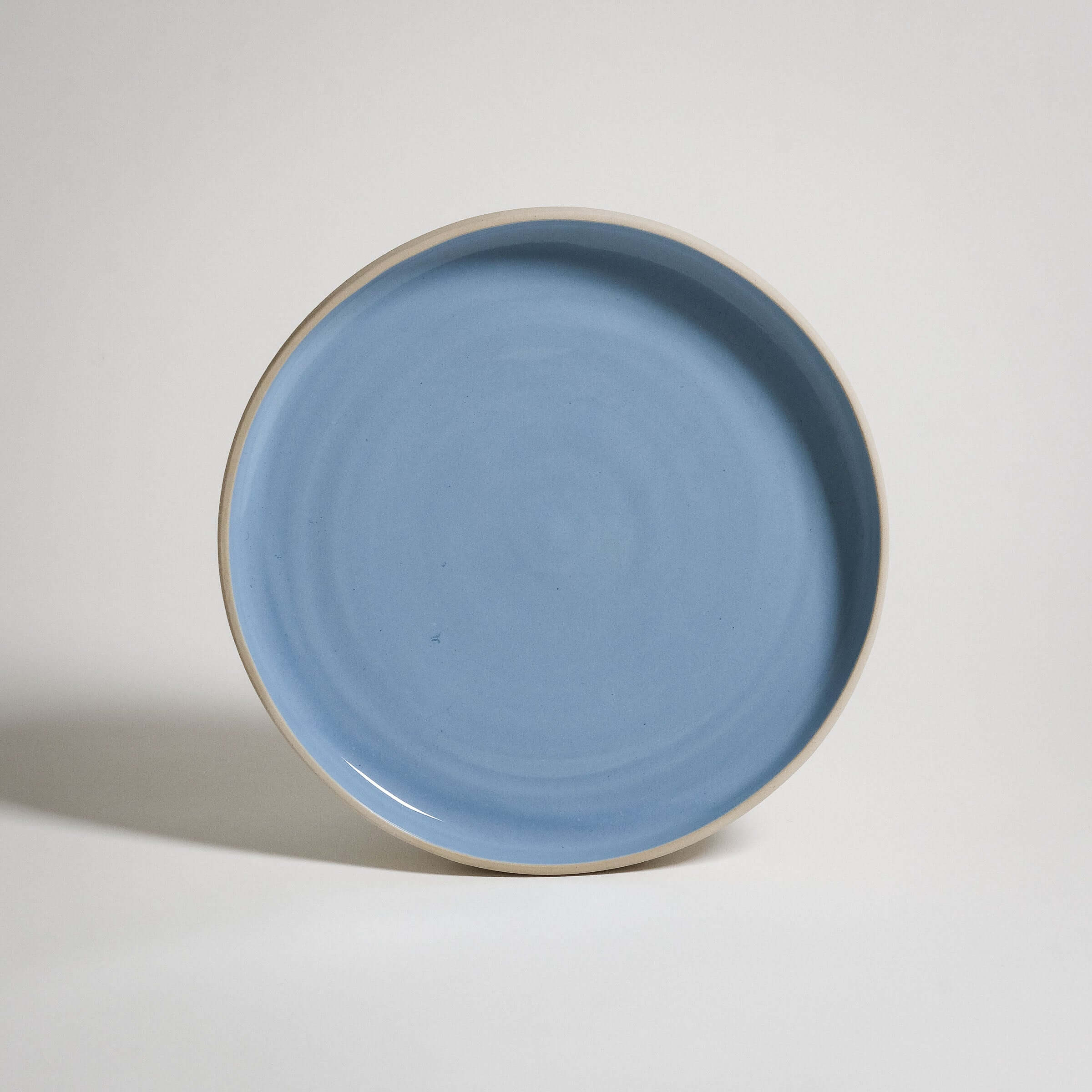 A Medium Plate with a higher rim. The outside is unglazed and the surface is glazed in blue glaizing