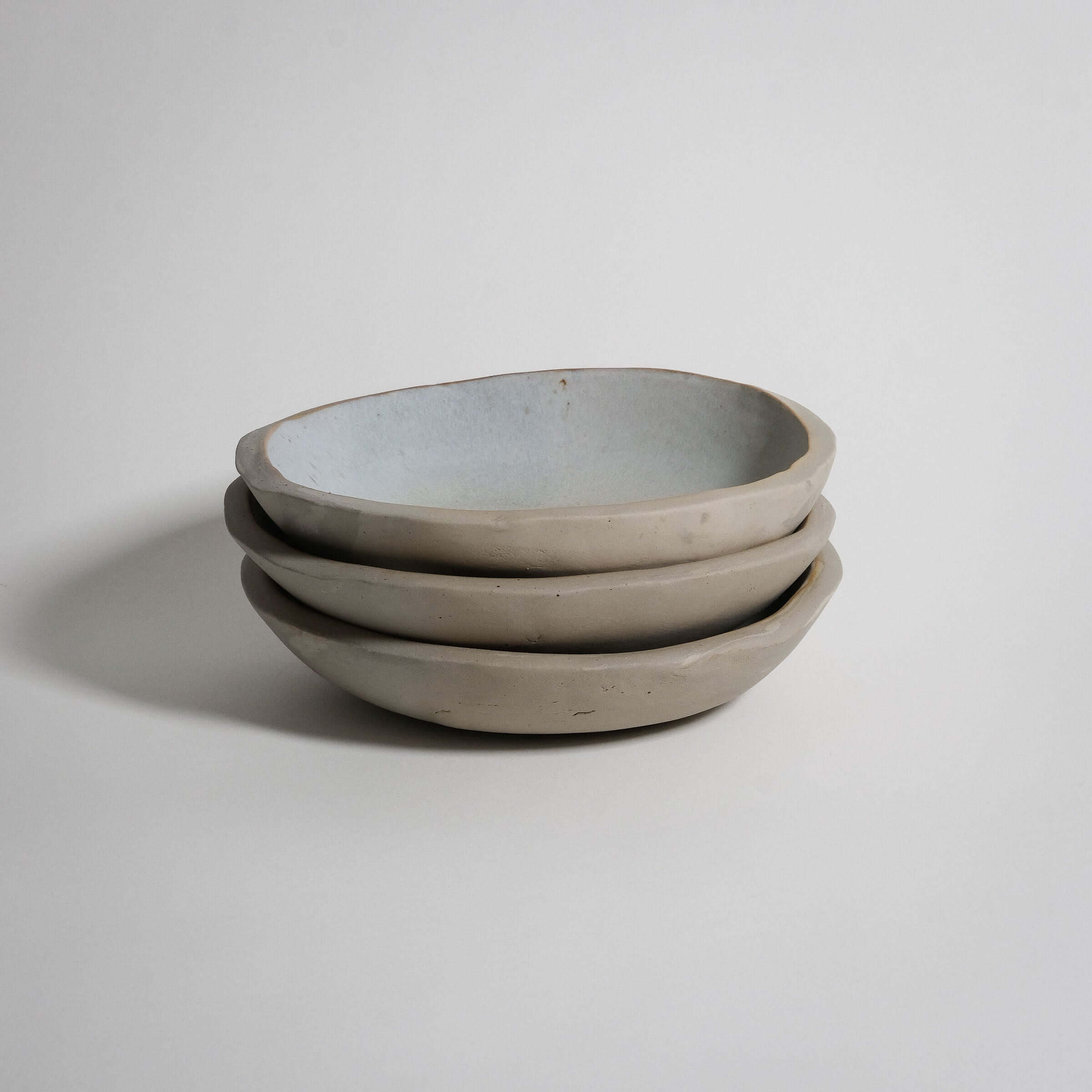 Handbuilt dinner bowls stacked, matte grey stoneware with food-safe matte white glaze inside.