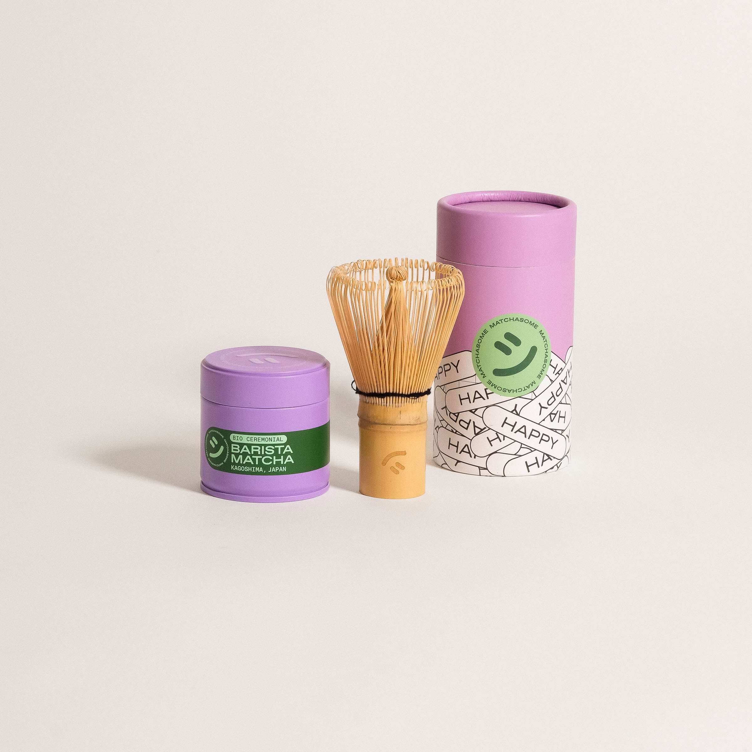 Bamboo matcha whisk with purple matcha containers, featuring a smiley logo and green labels, perfect for making foamy matcha.