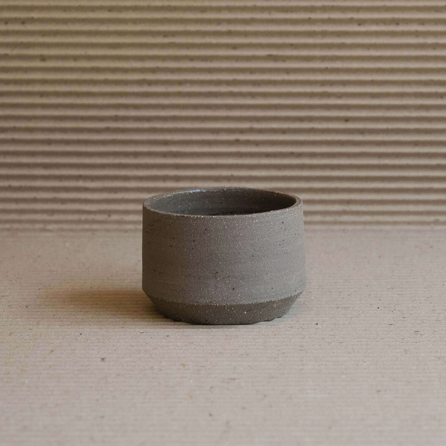 Handcrafted stoneware cup in gray, featuring raw exterior and glossy interior, showcasing unique clay textures.