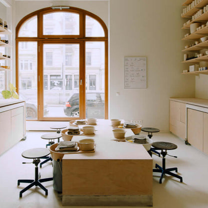Bright pottery studio with wooden tables, stools, and natural light for intimate class settings.