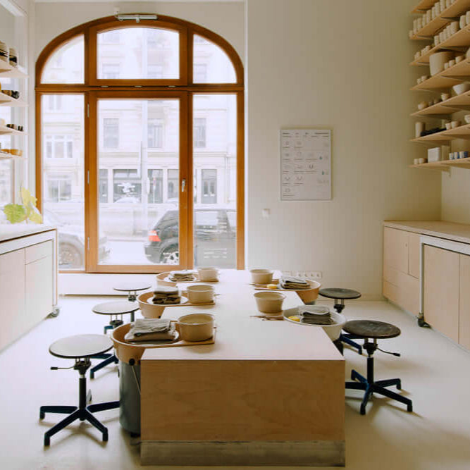 Bright pottery studio with wooden tables, stools, and natural light for intimate class settings.