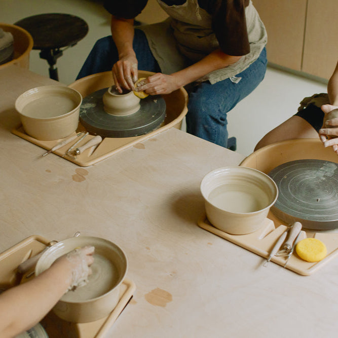 Beginners in a pottery wheel class shaping clay pieces during hands-on crafting sessions.