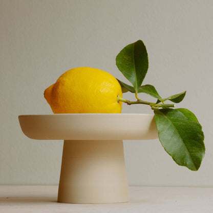 Aleah Bowl in grey stoneware featuring a lemon and a green branch, showcasing its unique pedestal design.