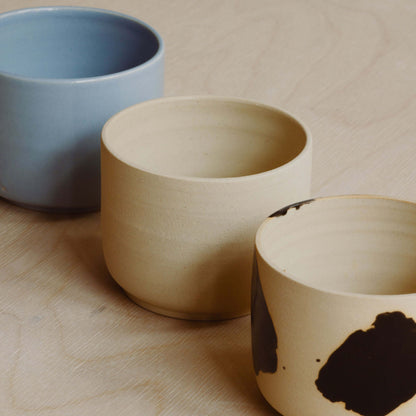 Three ceramic coffee cups are next two each other. One in iceblue, one in natural beige and one in natural beige with big black dots