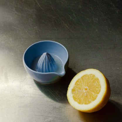 Handcrafted ice blue ceramic lemon juicer with fresh lemon on a metallic surface.