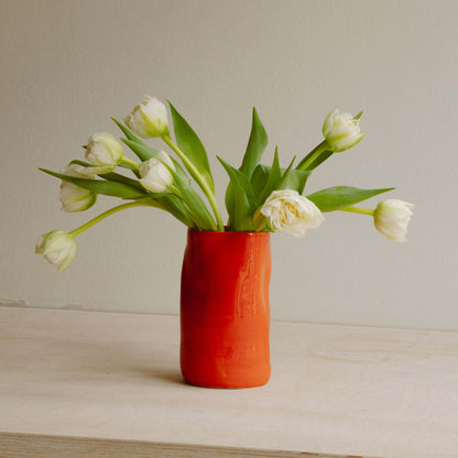 Handcrafted deep red stoneware vase filled with white tulips, showcasing a unique design perfect for any decor.