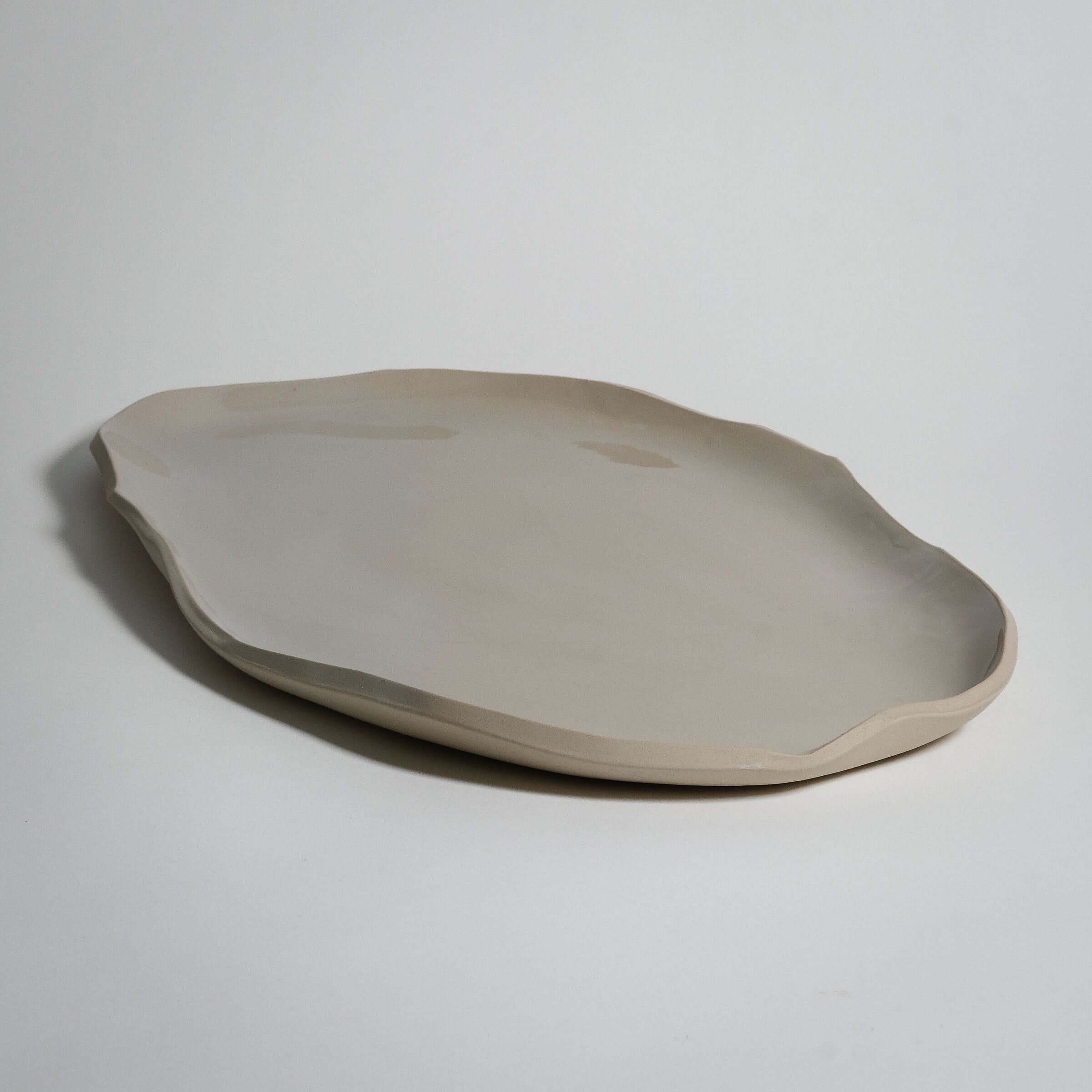 Wide serving tray in creme stoneware ceramic, featuring a unique shape and elegant transparent glaze, ideal for everyday use.