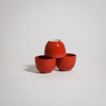 Three red ceramic espresso cups are stacked. Two are standing next to each other and one is upside down on top