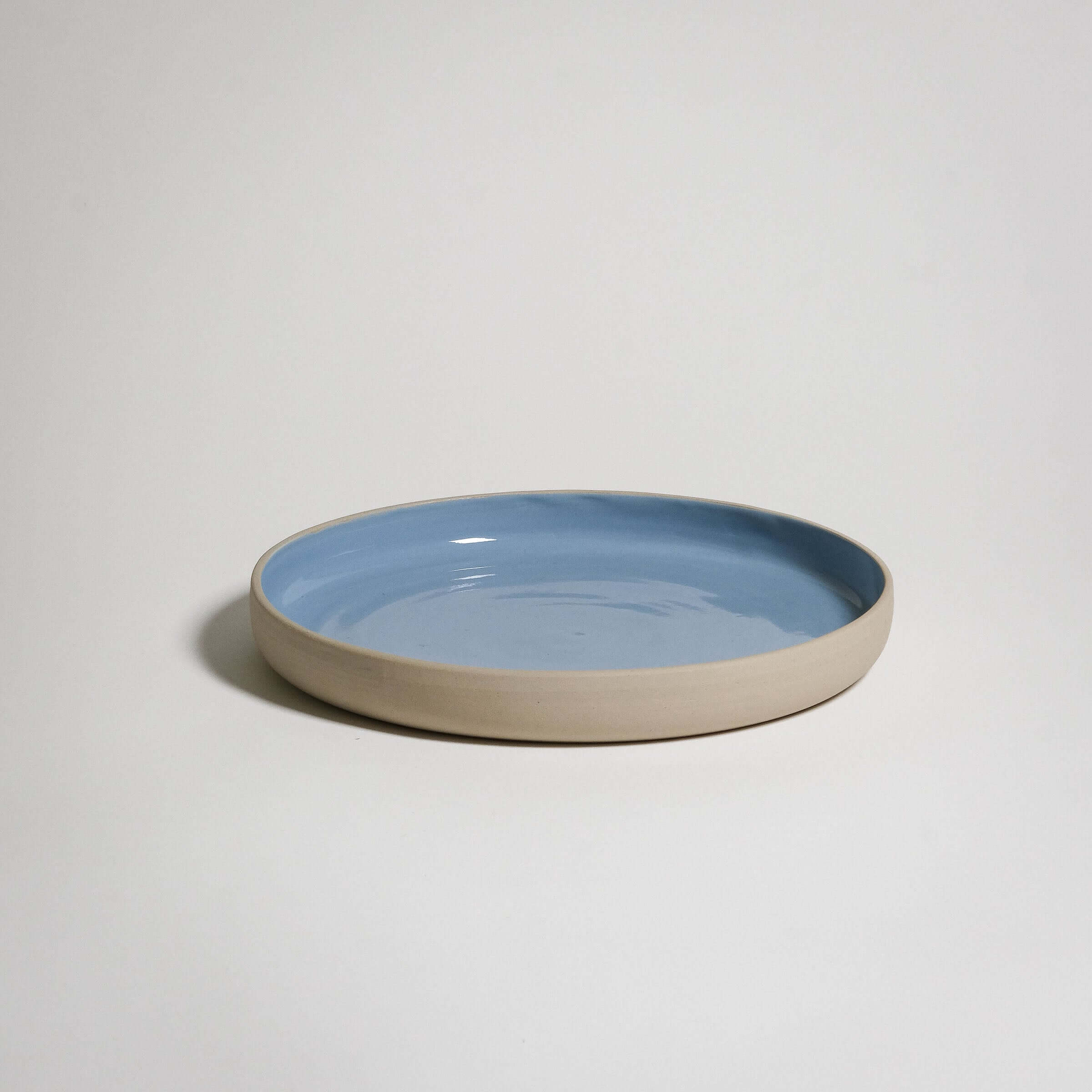 A Medium Plate with a higher rim. The outside is unglazed and the surface is glazed in blue glaizing