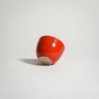 A red ceramic coffee cup side from the side, tilted a bit backwards