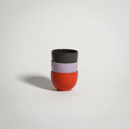 Set of three wheel-thrown espresso cups in red, lilac, and chocolate brown, fully glazed and stacked.