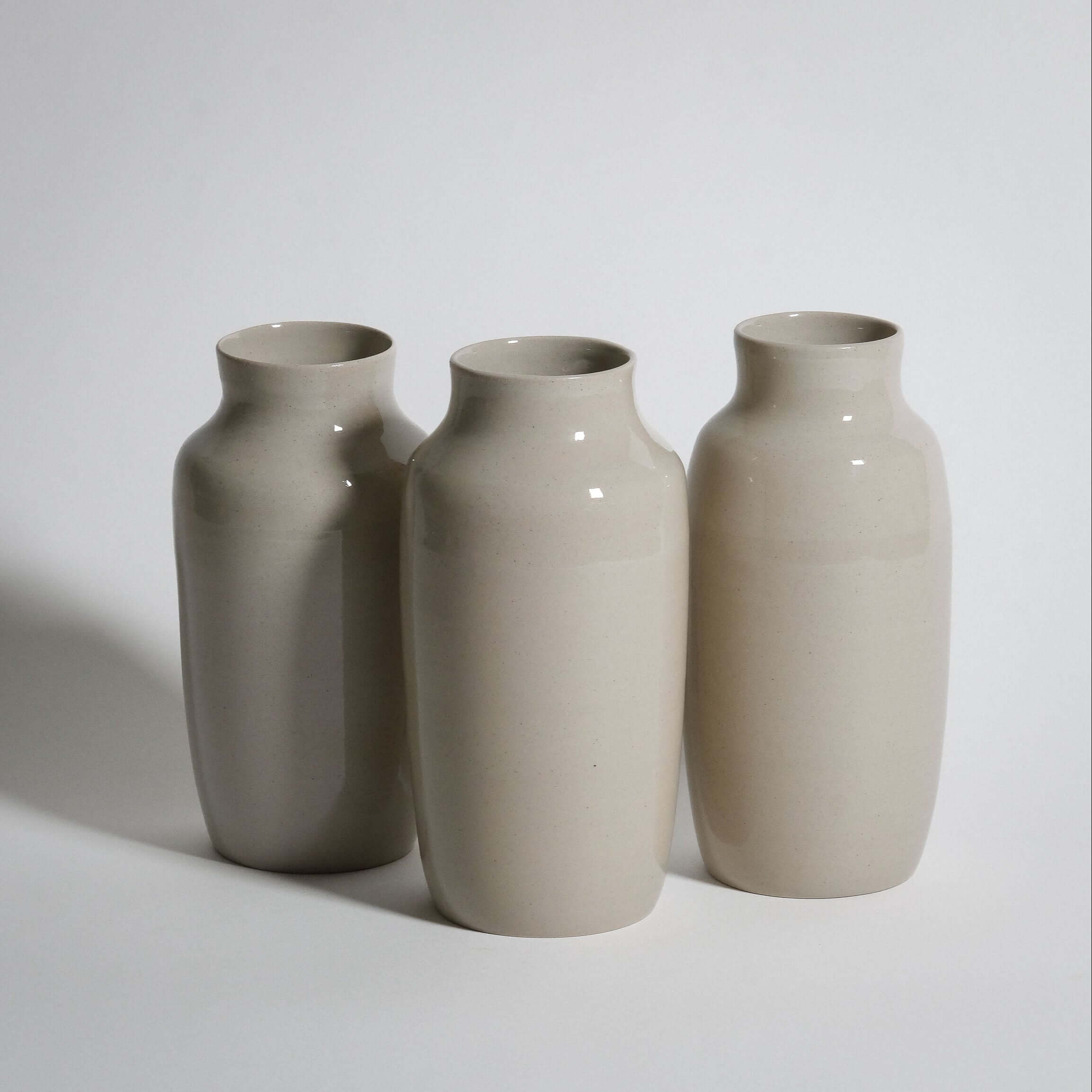 Set of three elegant handcrafted medium vases in creme color showcasing glossy stoneware finish.