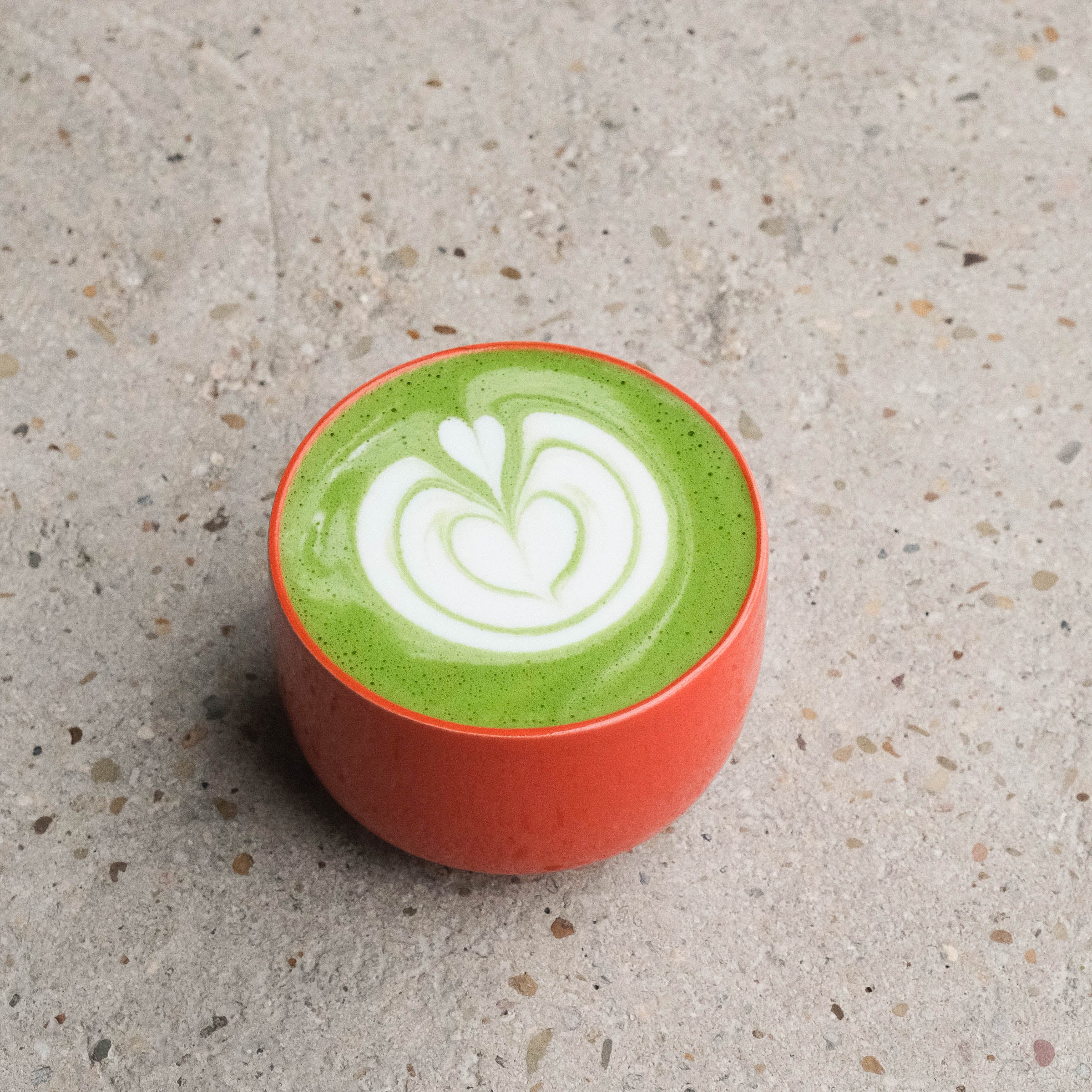 Glossy red matcha cup filled with vibrant green matcha and latte art on a textured surface.