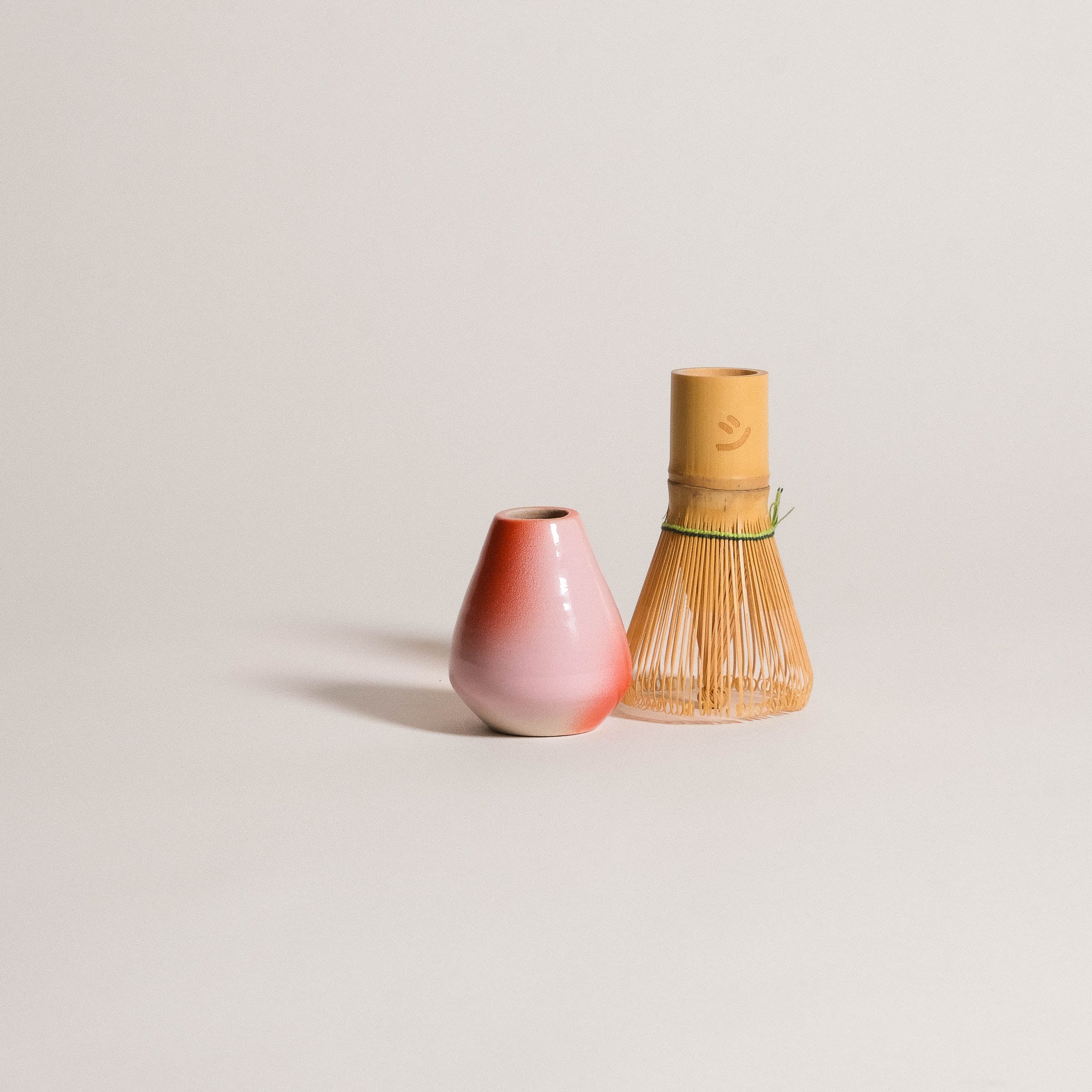 Matcha whisk holder in gradient pink-red stoneware beside a bamboo whisk, perfect for matcha tea rituals.