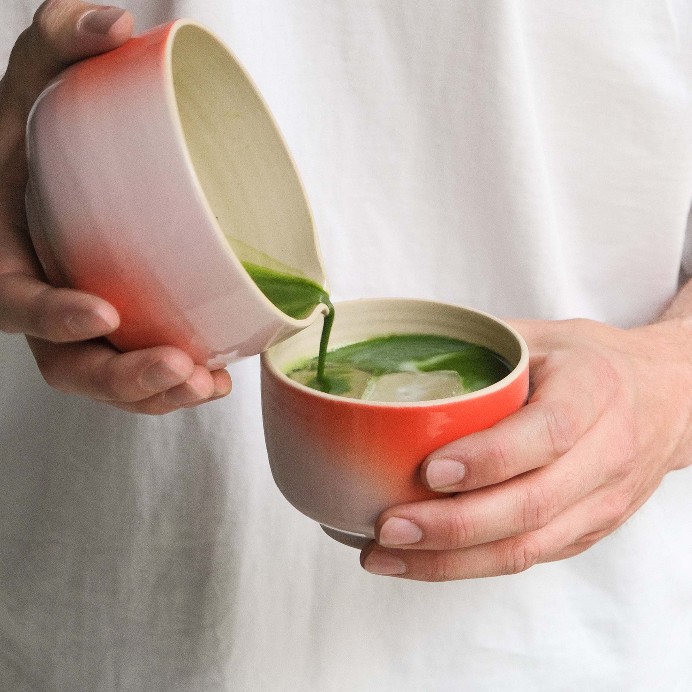 Person holding a matcha cup with a gradient design, pouring matcha into another cup, showcasing stoneware craftsmanship.