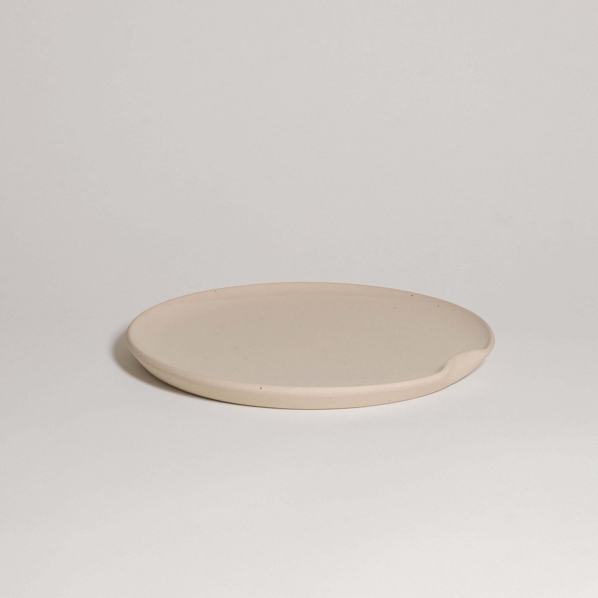 Flat creme dinner plate in grey stoneware with glossy surface, perfect for stylish dining and easy stacking.