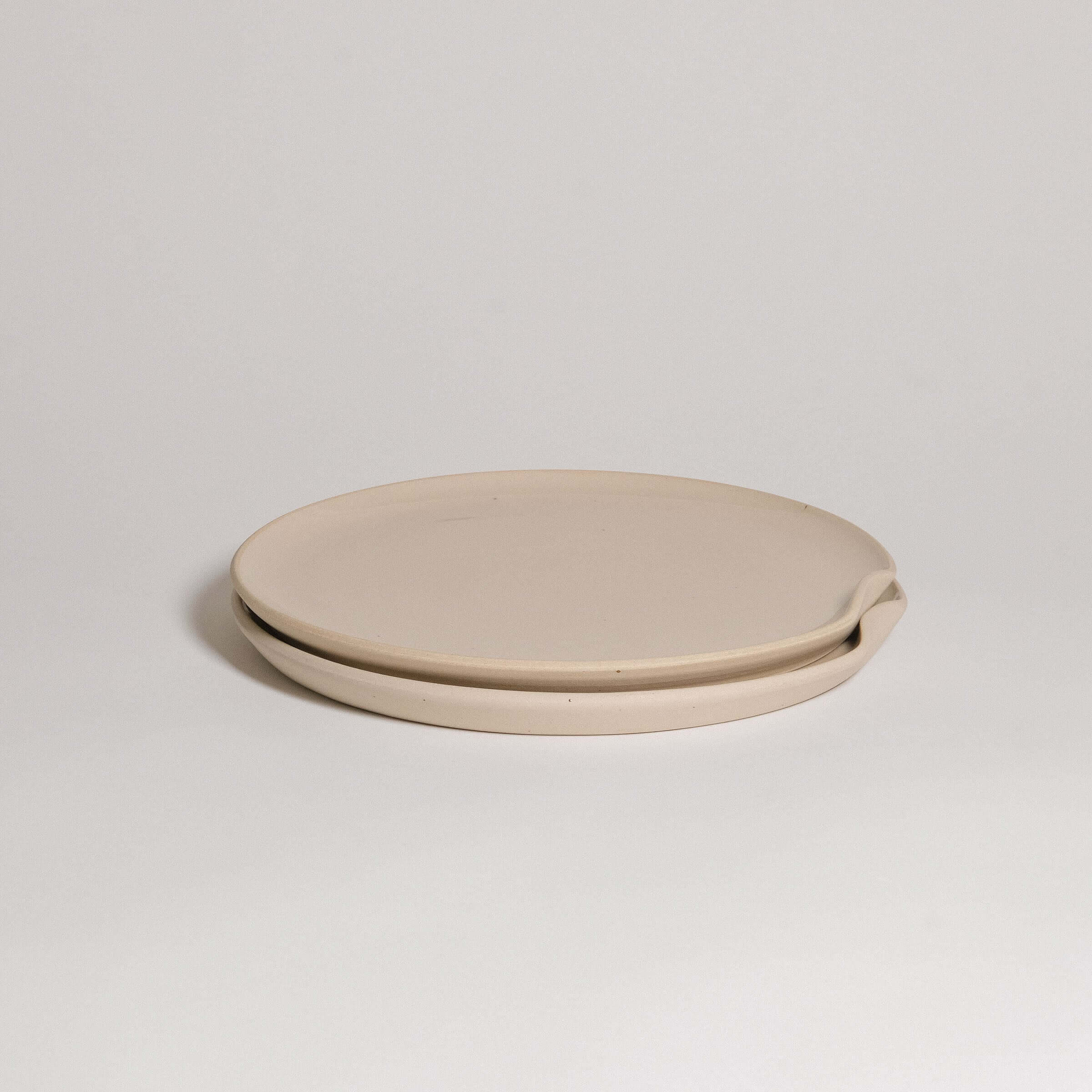 Limited edition grey stoneware dinner plate with glossy glaze, featuring a raw texture and easy stacking indentation.