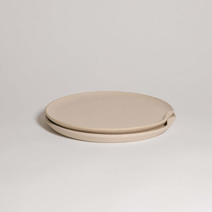 Limited edition grey stoneware dinner plate with glossy glaze, featuring a raw texture and easy stacking indentation.