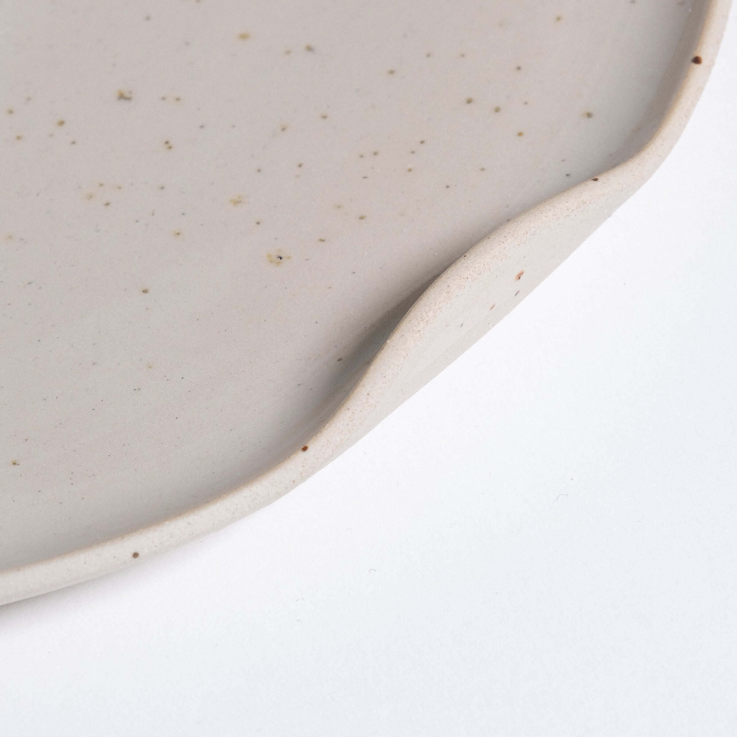 Close-up of a cream-colored stoneware dinner plate showcasing its smooth glazed interior and raw textured edge.